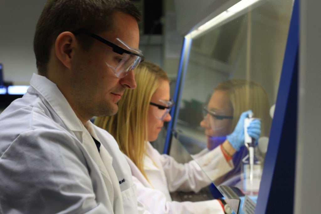 A man and woman wearing white laboratory coats are pipetting